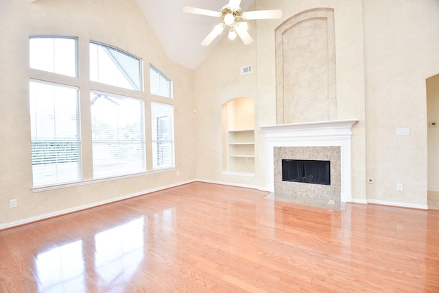 unfurnished living room featuring light wood-type flooring, ceiling fan, built in features, and high vaulted ceiling