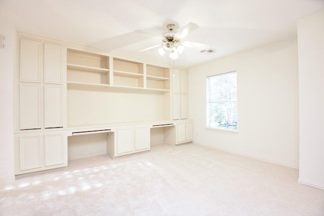 unfurnished office with light carpet, ceiling fan, and built in desk