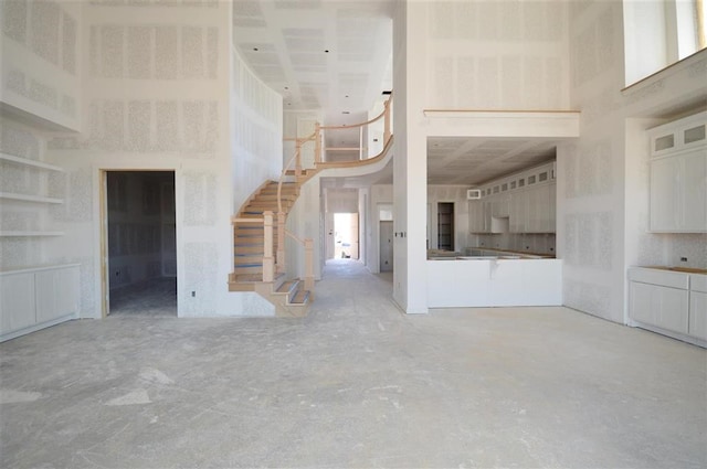 unfurnished living room featuring stairs and a high ceiling