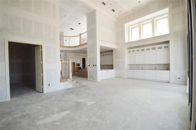 unfurnished living room featuring stairs, concrete floors, and a towering ceiling