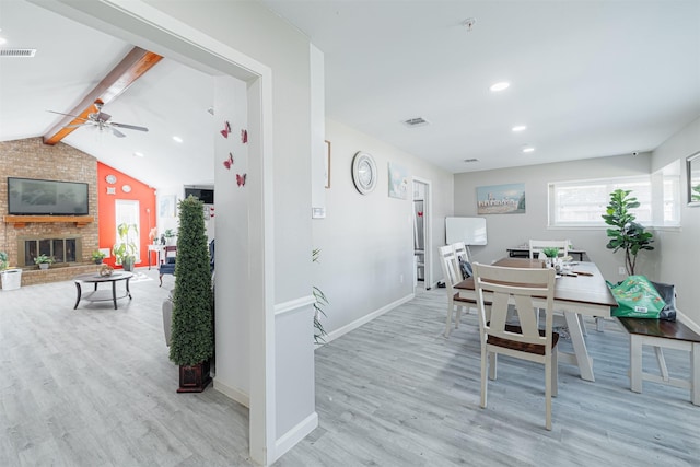 dining area with a brick fireplace, lofted ceiling with beams, light hardwood / wood-style floors, and ceiling fan