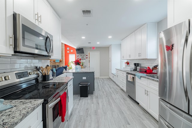 kitchen with light stone counters, tasteful backsplash, a kitchen island, stainless steel appliances, and white cabinets