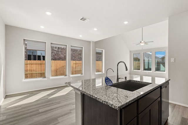 kitchen with dishwasher, light hardwood / wood-style flooring, sink, light stone counters, and a center island with sink