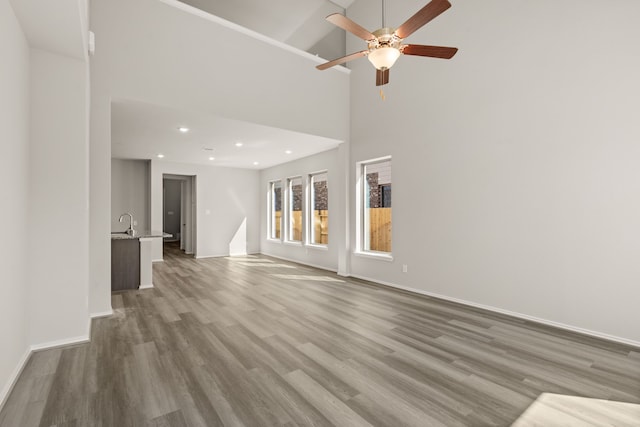 unfurnished living room with ceiling fan, sink, hardwood / wood-style floors, and a towering ceiling