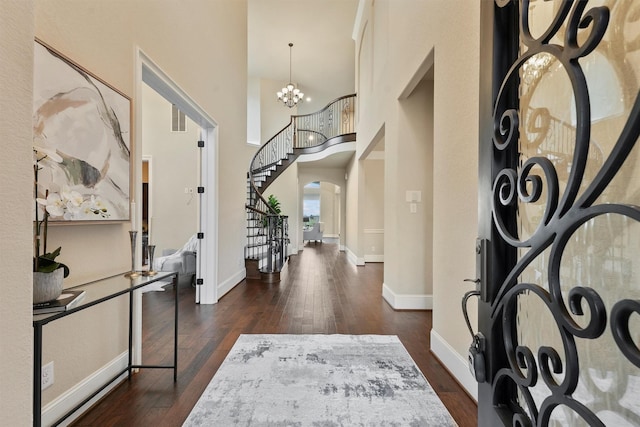 entrance foyer with dark hardwood / wood-style flooring, a towering ceiling, and a notable chandelier