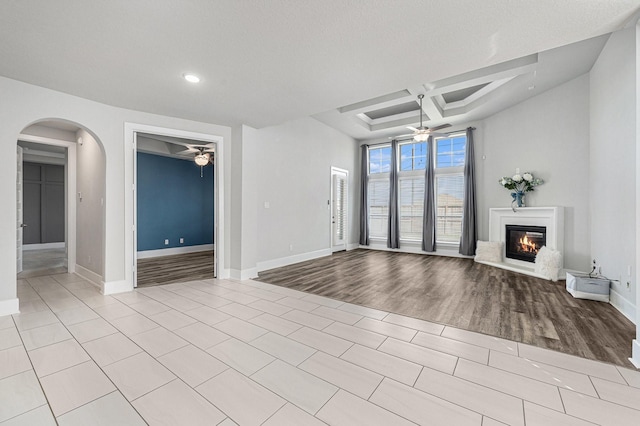 unfurnished living room featuring coffered ceiling, beamed ceiling, light tile patterned floors, and ceiling fan