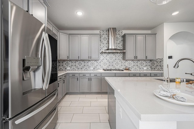 kitchen with appliances with stainless steel finishes, wall chimney range hood, tasteful backsplash, sink, and light tile patterned flooring