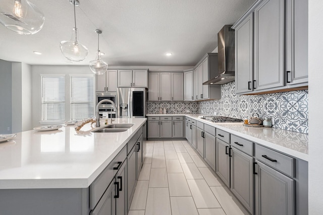 kitchen featuring hanging light fixtures, gray cabinetry, sink, stainless steel appliances, and wall chimney exhaust hood