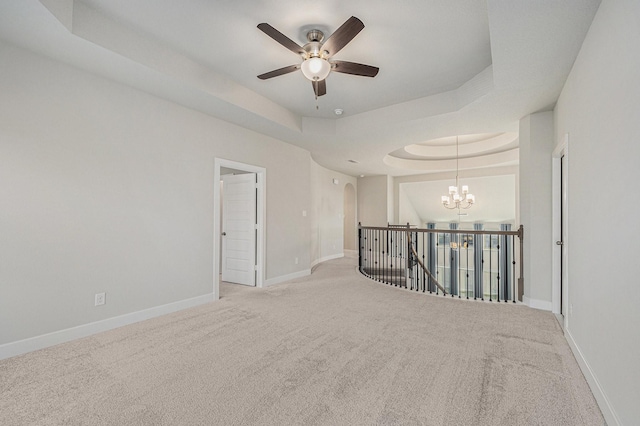 carpeted empty room featuring ceiling fan with notable chandelier and a tray ceiling