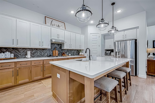 kitchen featuring appliances with stainless steel finishes, decorative light fixtures, white cabinetry, sink, and a center island with sink