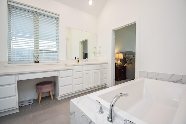 bathroom with vaulted ceiling, tile patterned floors, tiled tub, and vanity