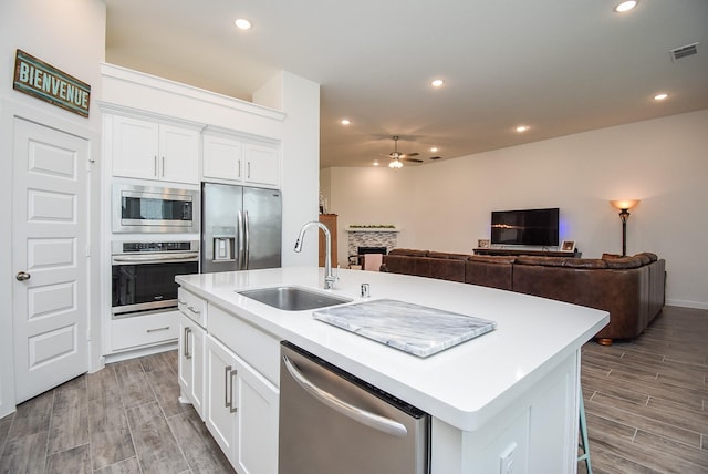 kitchen with white cabinets, sink, stainless steel appliances, and a center island with sink