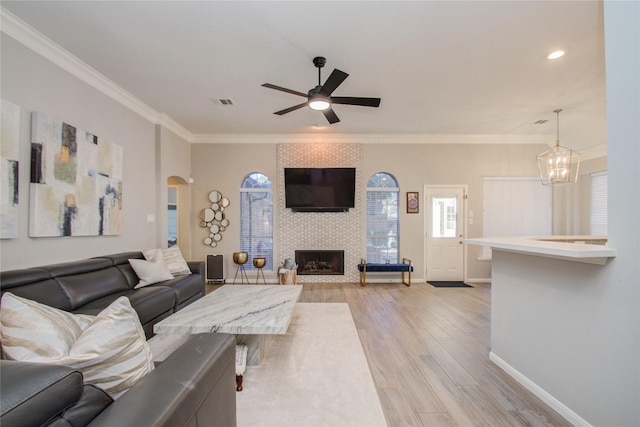 living room featuring a fireplace, ceiling fan with notable chandelier, ornamental molding, and light hardwood / wood-style floors