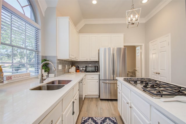 kitchen featuring white cabinetry, stainless steel appliances, a notable chandelier, decorative light fixtures, and sink