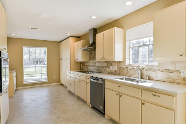 kitchen with backsplash, stainless steel dishwasher, sink, wall chimney exhaust hood, and cream cabinets