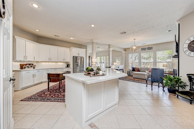 kitchen with white cabinets, a center island, ornate columns, stainless steel fridge, and light tile patterned floors