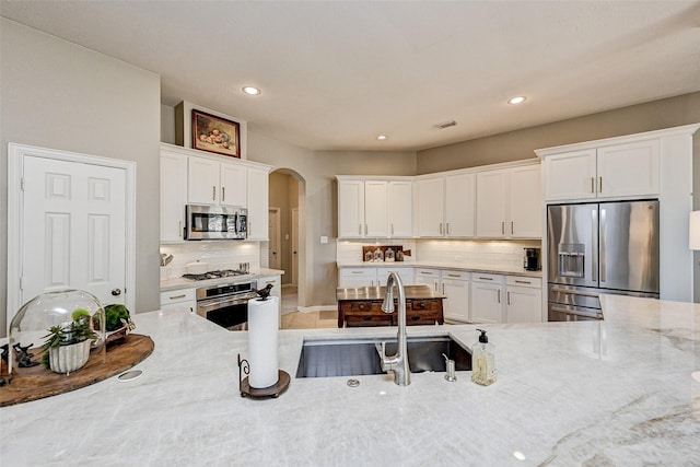 kitchen with sink, white cabinets, light stone counters, decorative backsplash, and stainless steel appliances