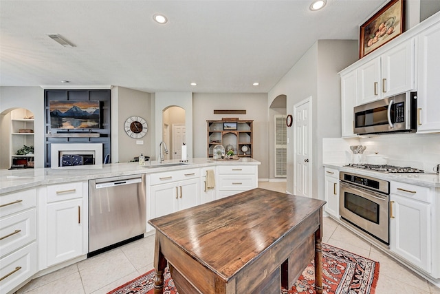 kitchen featuring appliances with stainless steel finishes, white cabinetry, kitchen peninsula, light stone counters, and light tile patterned floors