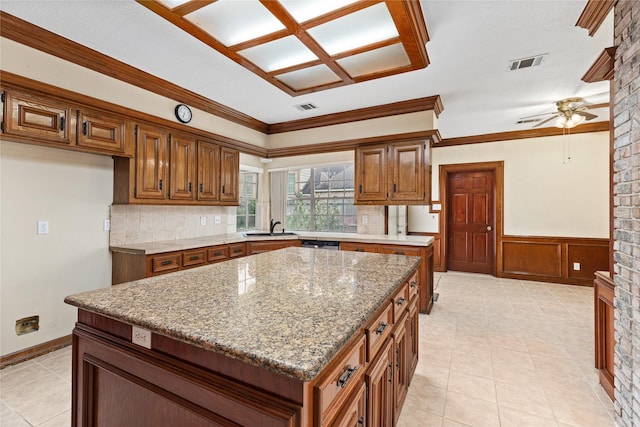 kitchen featuring a kitchen island, ceiling fan, sink, ornamental molding, and light stone counters