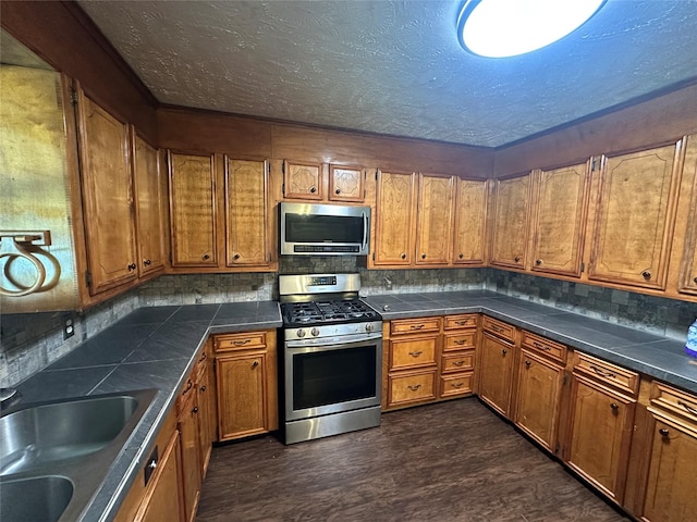 kitchen featuring a textured ceiling, appliances with stainless steel finishes, dark wood-type flooring, sink, and backsplash