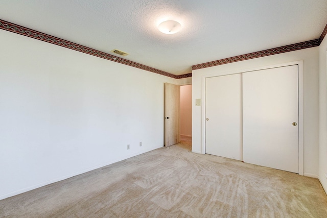 unfurnished bedroom featuring a closet, a textured ceiling, and light carpet