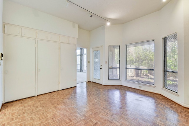 unfurnished bedroom featuring a high ceiling, rail lighting, and light parquet flooring