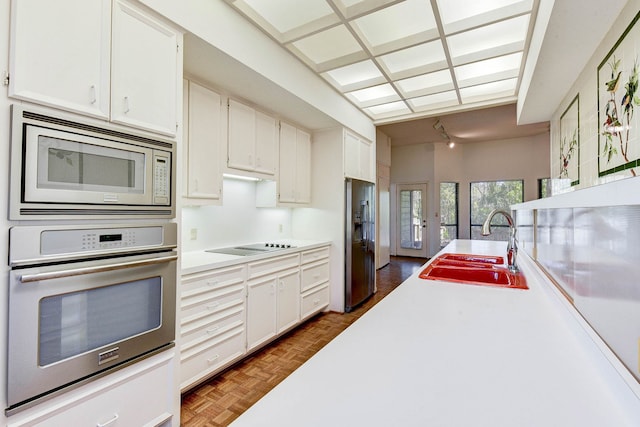 kitchen with white cabinets, stainless steel appliances, dark parquet flooring, and sink