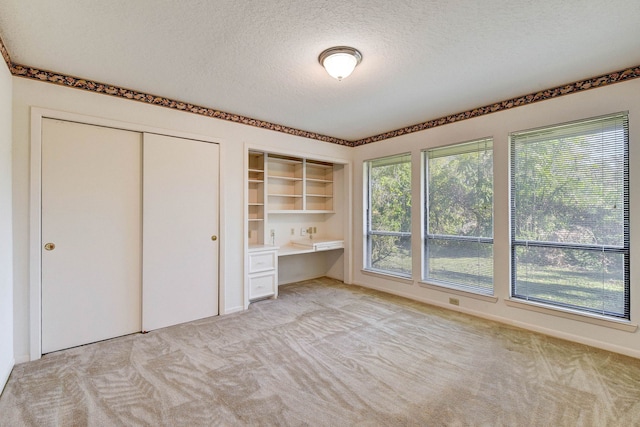 unfurnished bedroom featuring light colored carpet, a textured ceiling, and built in desk