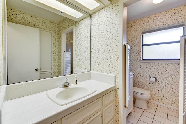 bathroom with toilet, vanity, a skylight, and tile patterned flooring