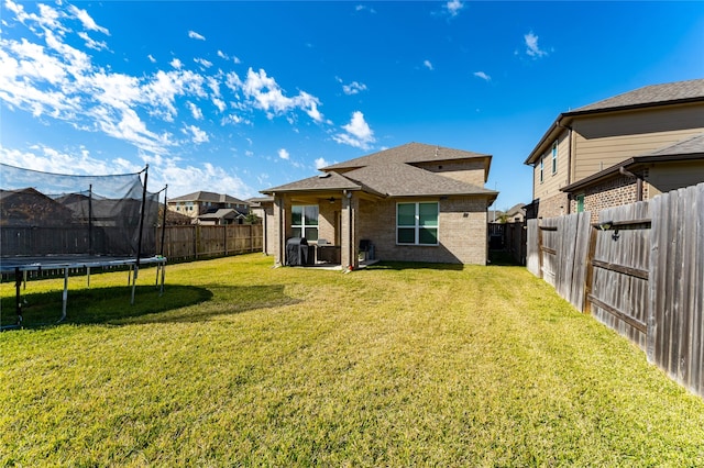 back of property featuring a lawn and a trampoline