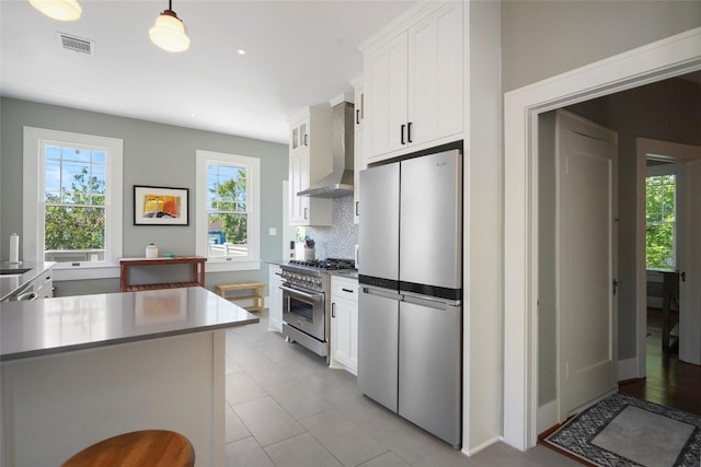 kitchen featuring decorative light fixtures, white cabinets, appliances with stainless steel finishes, and wall chimney exhaust hood