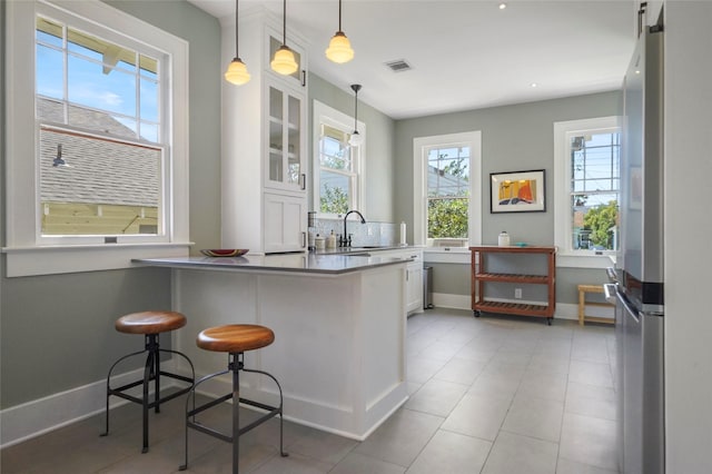 kitchen with pendant lighting, white cabinetry, a kitchen breakfast bar, kitchen peninsula, and stainless steel refrigerator