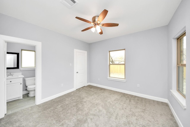 unfurnished bedroom featuring sink, multiple windows, ensuite bathroom, and ceiling fan