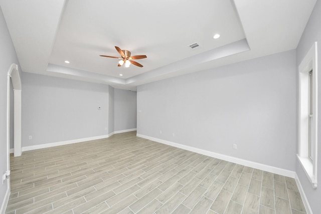 unfurnished room with ceiling fan, a raised ceiling, and light wood-type flooring