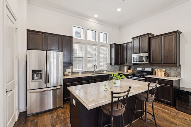 kitchen with light stone countertops, a kitchen island, a kitchen bar, stainless steel appliances, and sink