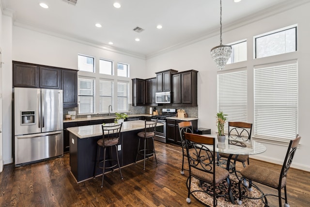 kitchen featuring pendant lighting, dark wood-type flooring, ornamental molding, a kitchen island, and stainless steel appliances