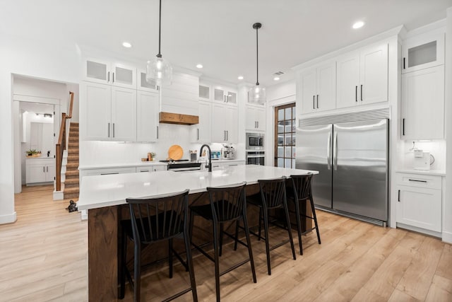 kitchen with built in appliances, white cabinetry, and pendant lighting