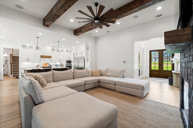 living room with sink, light hardwood / wood-style flooring, beamed ceiling, and a fireplace