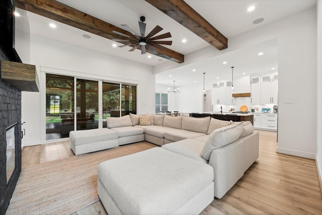 living room with ceiling fan with notable chandelier, light hardwood / wood-style flooring, beam ceiling, and a fireplace