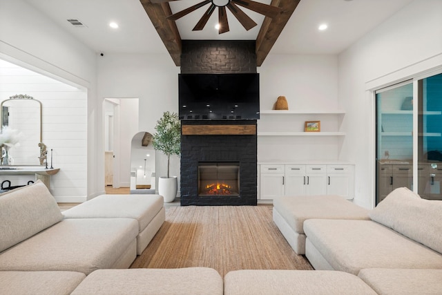 living room featuring light hardwood / wood-style floors, beamed ceiling, ceiling fan, and a large fireplace