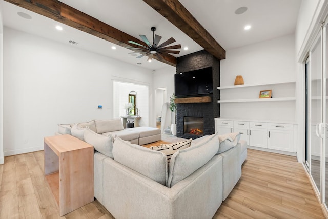 living room featuring light wood-type flooring, ceiling fan, beam ceiling, and a fireplace