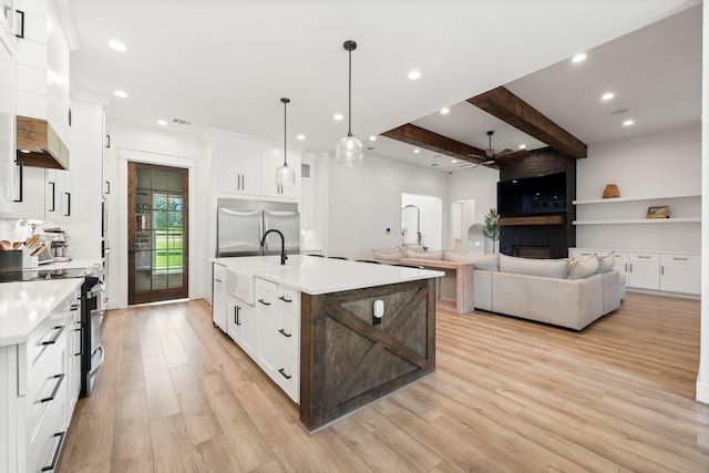 kitchen featuring pendant lighting, appliances with stainless steel finishes, white cabinets, beam ceiling, and a kitchen island with sink