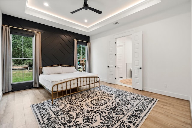 bedroom with hardwood / wood-style flooring, multiple windows, ceiling fan, and a raised ceiling