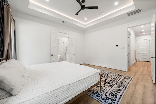 bedroom featuring ceiling fan, light hardwood / wood-style flooring, connected bathroom, and a tray ceiling