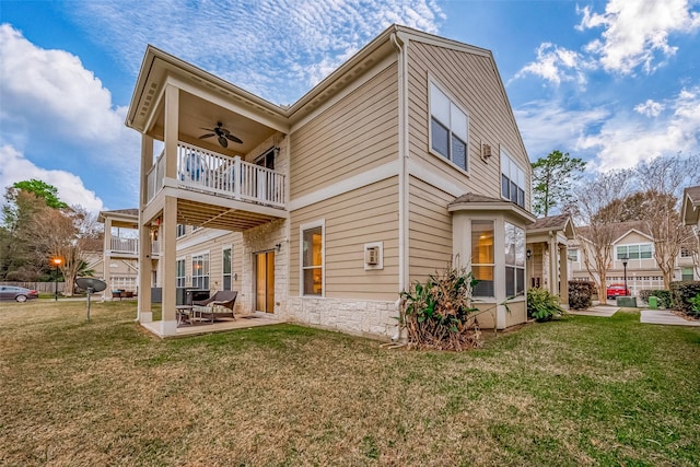 rear view of property with a balcony, a yard, ceiling fan, and a patio