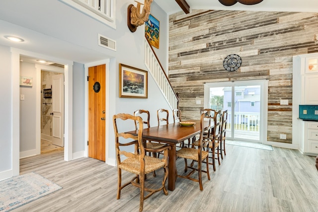 dining area featuring beam ceiling, light hardwood / wood-style flooring, high vaulted ceiling, and wooden walls