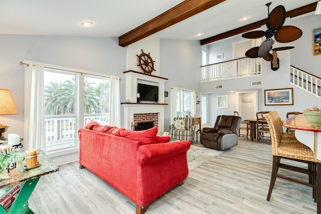 living room with a brick fireplace, vaulted ceiling with beams, ceiling fan, and light hardwood / wood-style flooring