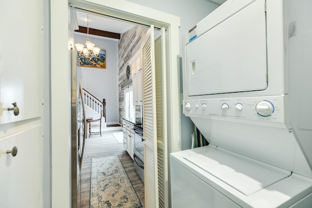 laundry area with stacked washer and clothes dryer, a chandelier, and hardwood / wood-style floors