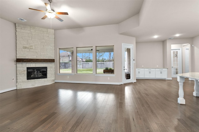 unfurnished living room with ceiling fan, dark hardwood / wood-style floors, and a stone fireplace