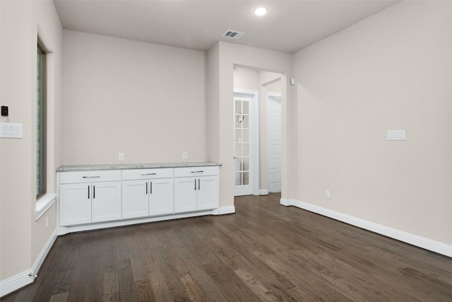 interior space with white cabinets, dark wood-type flooring, and light stone counters